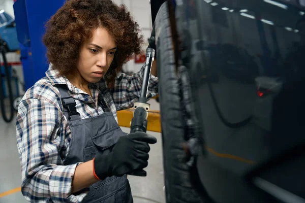 Młody Mechanik Ubraniu Roboczym Patrzy Koło Samochodu Kobieta Pracuje Nowoczesnym — Zdjęcie stockowe