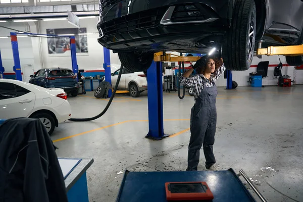 Wielorasowy Kobieta Mechanik Stoi Pod Samochodem Bada Dołu Samochód Jest — Zdjęcie stockowe