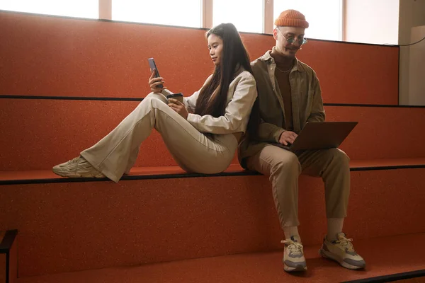 Jovem Focada Lendo Algo Celular Enquanto Cara Satisfeito Trabalhando Laptop — Fotografia de Stock