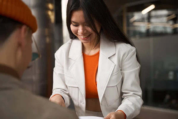 彼女の白人同僚に文書を示す幸せなアジアの女性オフィス労働者を微笑む — ストック写真