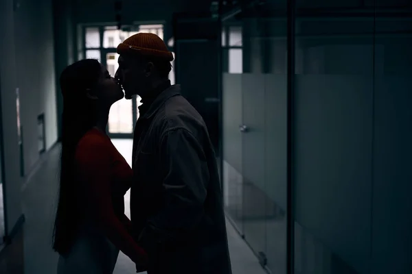 サイドビューの若いです男と女接吻オン唇で暗い廊下 — ストック写真