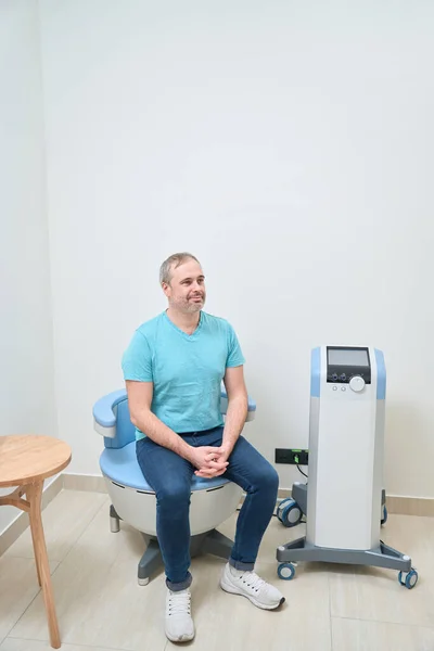 Smiling Caucasian male patient waiting for doctor while sitting on exam room