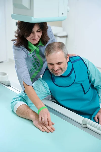 Médico Sonriente Corrigiendo Mano Del Paciente Mientras Ayuda Hacer Rayos — Foto de Stock