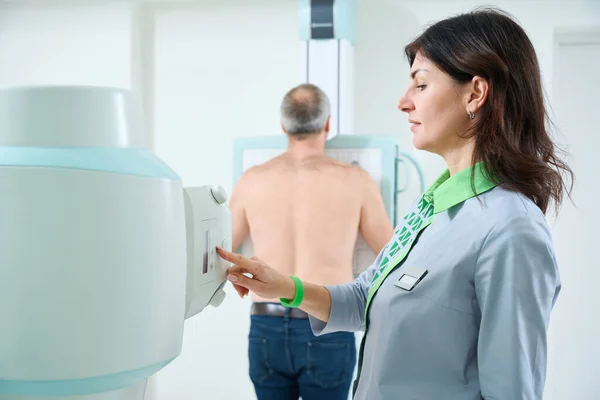 엑스선 기계를 작동하는 동안에 남자의 엑스선 사진을 미소짓는 방사선 전문의 — 스톡 사진