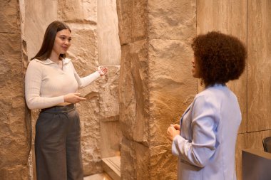 İş elbiseli hoş bir kadın lobide kıvırcık saçlı müşteriye nereye gideceğini anlatıyor.