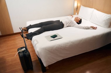 Sakin, rahat bir genç kadın otel odasında gözleri kapalı bir şekilde yatıyor.