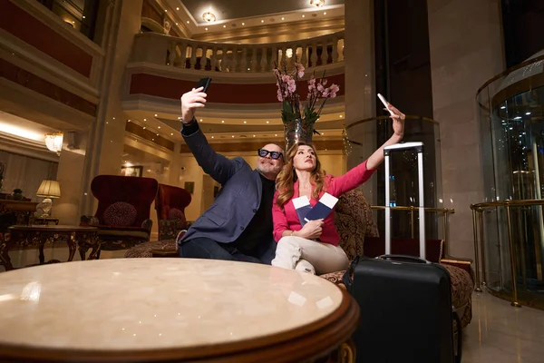 这对年轻漂亮的夫妇在宾馆的大堂里自拍 夫妻们坐在一个舒适的座位上 — 图库照片