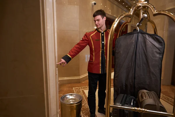 年轻的行李员推着一辆装有行李的购物车绕着大厅转 那人按下电梯按钮 — 图库照片