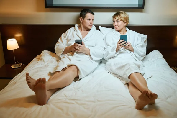 Man Woman Bathrobes Sitting Large Bed Have Mobile Phones Hands — Stock Photo, Image