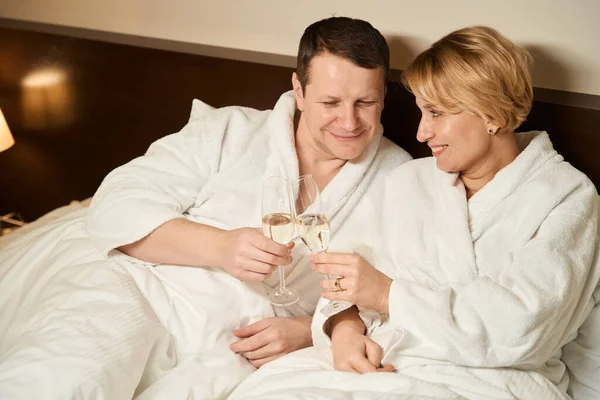 中年の男性と女性はベッドの中でシャンパンを楽しむ カップルは大きなベッドの上に定住 — ストック写真