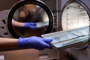Doktor eldivenlerini özel bir ızgarada tutuyor ve sterilizasyon için otoklavın içine yerleştiriyor.