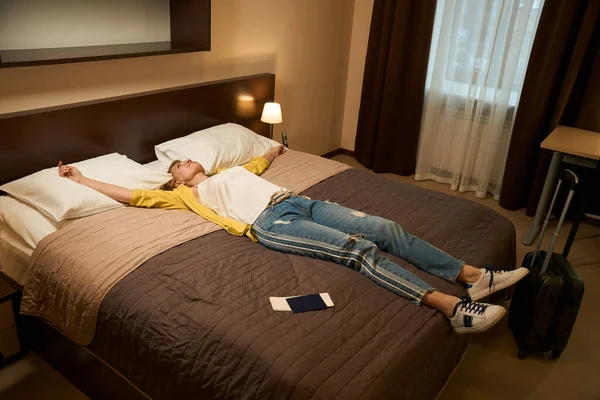 Blondynka Podróżnym Ubraniu Leży Dużym Łóżku Wyciągnięte Ramiona Paszport Bilet — Zdjęcie stockowe