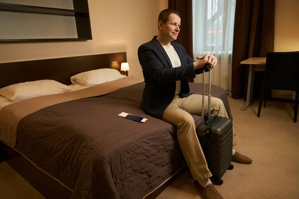旅行用のスーツケースを着た男性がホテルの部屋のベッドルームに座っています — ストック写真