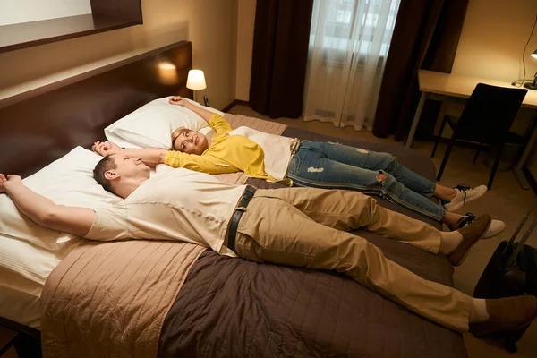 幸せな夫婦は大きなホテルのベッドの上の道路から休んでいる 配偶者はお互いに笑っている — ストック写真