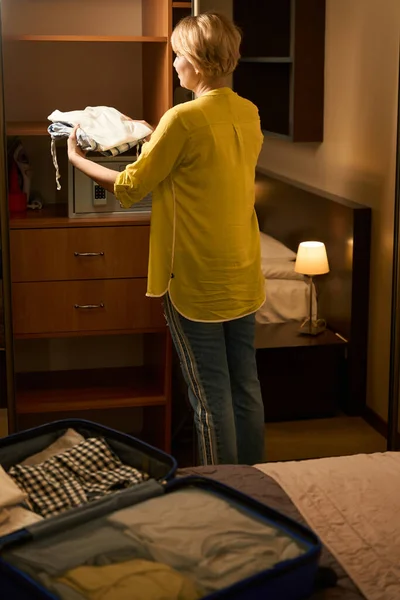 穿牛仔裤的女人把旅行箱里的衣服放在衣橱里 手提箱放在一张大床上 — 图库照片