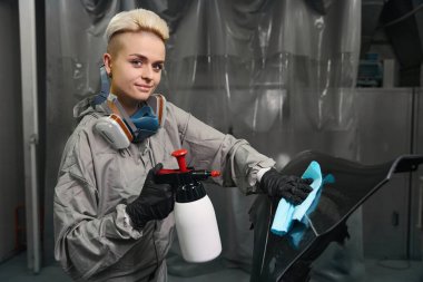 Koruyucu üniformalı kadın işçinin, dezenfeksiyon odasındaki vücut unsurlarını temizlerken kameraya bakması.