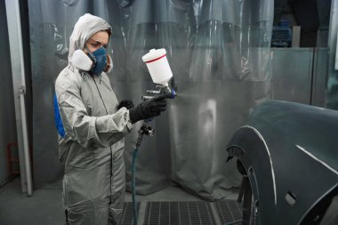 Korumalı iş kıyafetlerinde profesyonel kadın mühendis servis garajında boya sıkarken düşüncelere daldı.