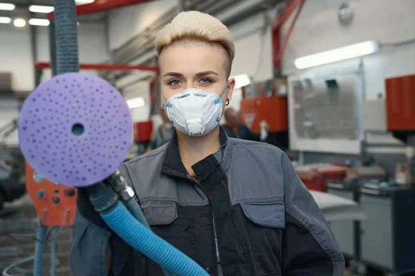 自動車修理工場で車を研磨するためのマスクと安全手袋を保持電気機械を身に着けている女性技術者の肖像 — ストック写真