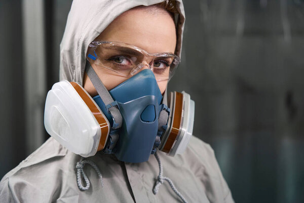 Close up view of woman in respirator and goggles looking at camera with serious facial expression indoors