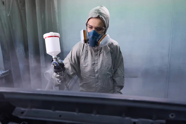塗装室で車体要素に取り組む保護具を身に着けている女性の自動車技術者 — ストック写真
