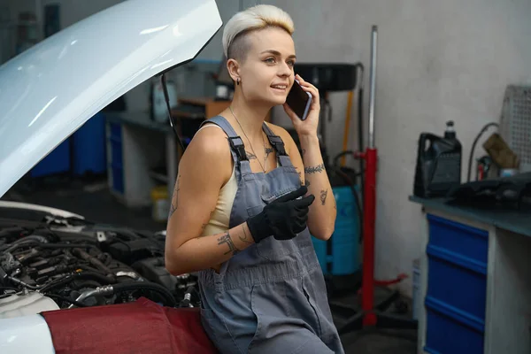 Woman in an auto repair shop is talking on the phone, the craftswoman has a stylish short haircut