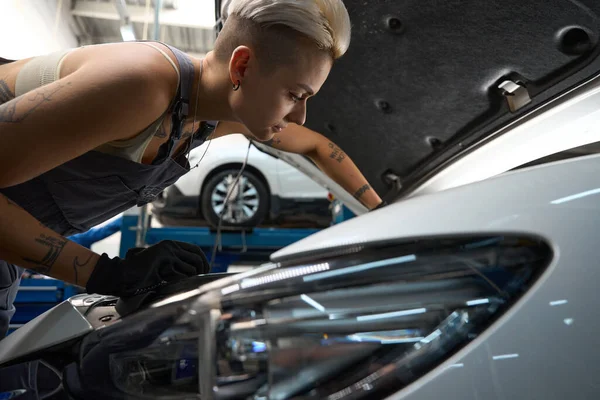 Genç Kadın Oto Tamircisi Arabanın Motorunu Kontrol Ediyor Dövmeli Tulumlu — Stok fotoğraf