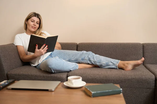 Charmoso Feminino Descansando Sofá Confortável Livro Leitura Entusiasticamente Sala Estar — Fotografia de Stock