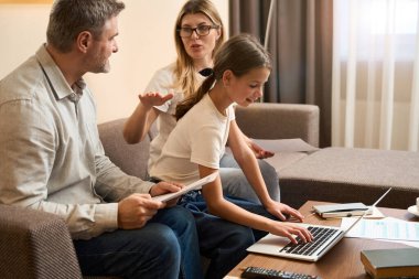 Küçük kız laptopunu kullanırken düşünceli anne ve babası dairede birbirleriyle konuşuyorlardı.