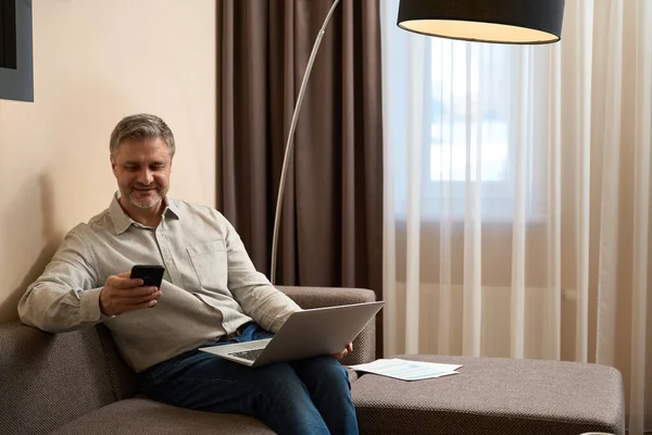Bonito Homem Sentado Sofá Com Laptop Suas Pernas Enquanto Usa — Fotografia de Stock