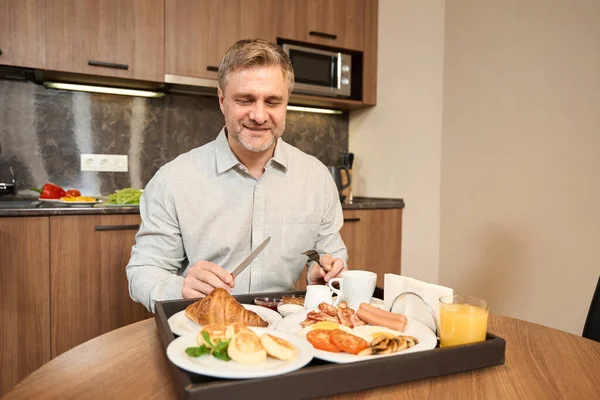 一个成年人坐在厨房的桌子旁边 面前摆着一个盘子 上面有各种各样的好吃的早餐 — 图库照片