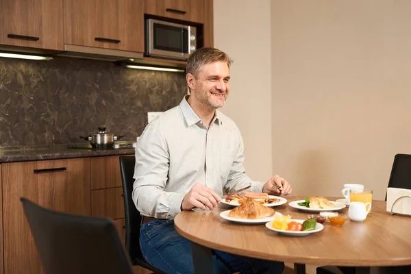 Gülümseyen Adam Mutfakta Masada Oturuyor Kahvaltıda Bir Sürü Lezzetli Yemek — Stok fotoğraf