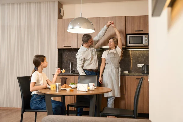 Niña Está Sentada Mesa Comiendo Bebiendo Sus Padres Bailando Cocina — Foto de Stock