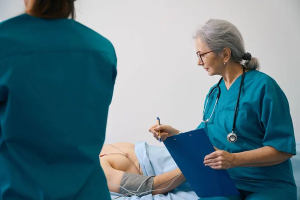 女医务工作者用现代设备对病人进行检查 旁边站着一名助手 — 图库照片