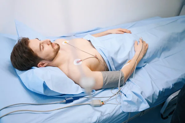 心臓科で検査中の若い男は患者モニターに接続されてる — ストック写真