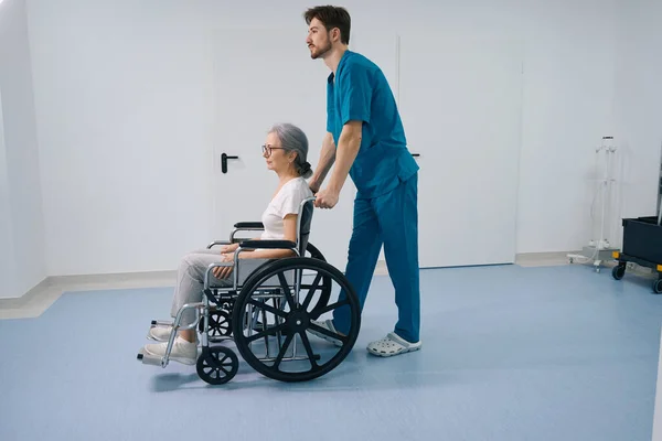 Pečující Sestra Nese Starší Dámu Invalidním Vozíku Chodbě Nemocnice Pokoj — Stock fotografie