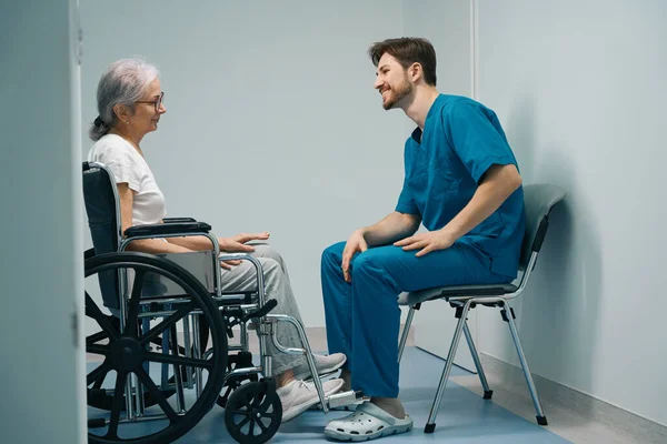 Orvosi Egyenruhás Férfi Kommunikál Egy Tolószékes Idős Beteggel Embereket Kórházi — Stock Fotó