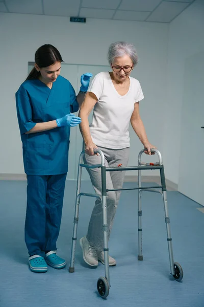 一位年轻的护士陪着一位老太太 病人与一位散步者同行 — 图库照片