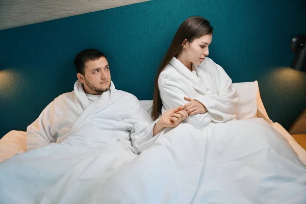 心情不好的年轻女人正坐在一张大床上 她长胡子的丈夫正设法与她和好 — 图库照片