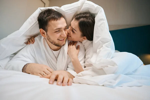 夫で愛抱擁とささやき下にカバー上の大規模なベッド 男で柔らかいバスローブ — ストック写真