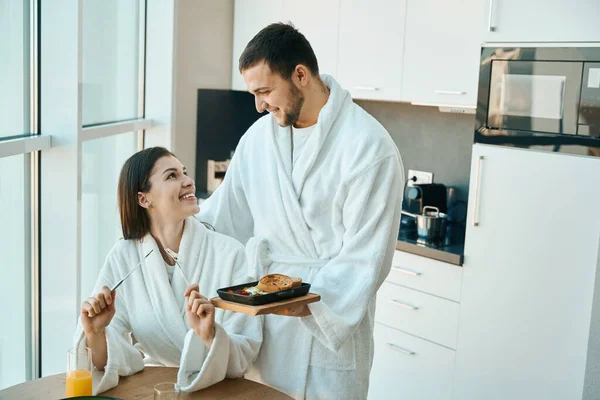 有爱心的年轻丈夫在舒适的气氛中招待他迷人的妻子吃早餐 男人们穿着舒适的浴衣 — 图库照片