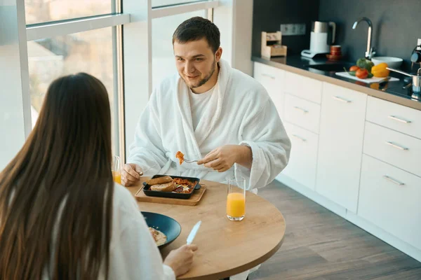 年轻的夫妻们在舒适的气氛中享用早餐时聊得很惬意 男人们穿着柔软的浴衣 — 图库照片