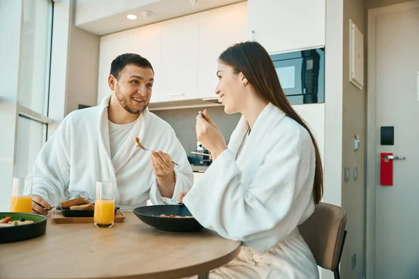 幸せな若いカップルが居心地の良い環境で朝食を持っている 柔らかいバスローブの男 — ストック写真