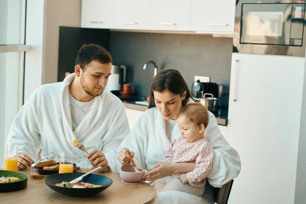 在一个阳光明媚的早晨 一个年轻的家庭在厨房桌上吃早餐 — 图库照片