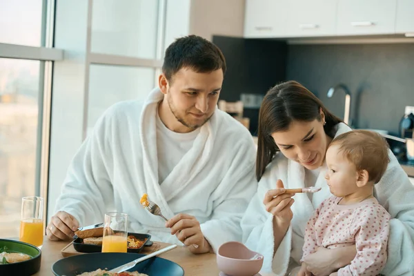 快乐美丽的女人正在喂她的小女儿 爸爸和一个小孩正在吃早饭 — 图库照片