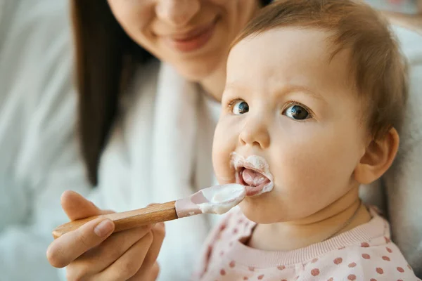 小さなスプーンで小さな子供を養う笑顔の女性 赤ちゃんはぽっちゃり頬を持っています — ストック写真