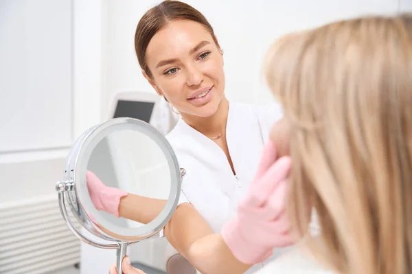 美容師と相談して美容医学のクリニックの依頼人女性は鏡を見る — ストック写真