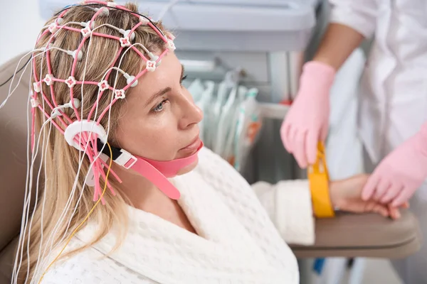 stock image Diagnostician in the rehabilitation center prepares the patient for the electroencephalogram procedure, female in a cap with electrodes