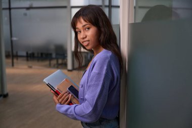 Koridorda iş için elinde eşyalar tutarken kameraya bakan şık elbiseli hoş bir kadın.