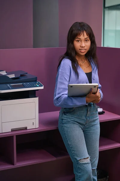Attractive female employee in fancy clothes holding laptop while standing near workplace in modern room