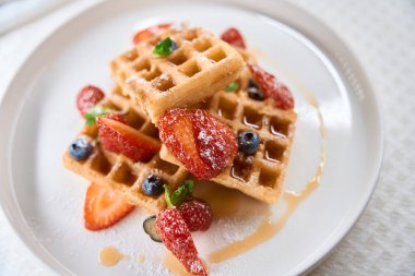 Tatlı soslu taze Belçika waffleları ya da bal ve mevsimlik böğürtlen tabakta servis edilir, yakın plan.